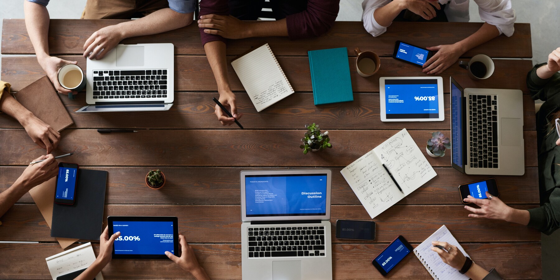 overhead view of people sitting at a table with laptops, tablets and phones