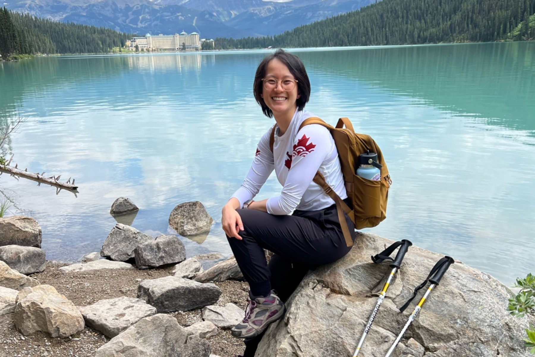 Samantha Li sitting in front of a lake with mountains in the background.