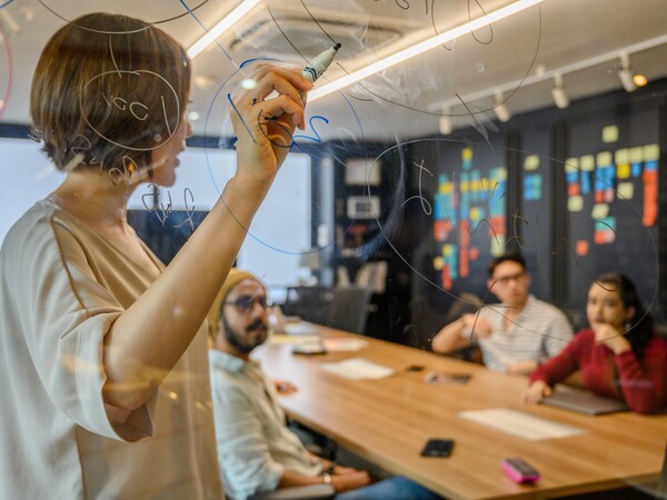 a person writes on a white board during a meeting