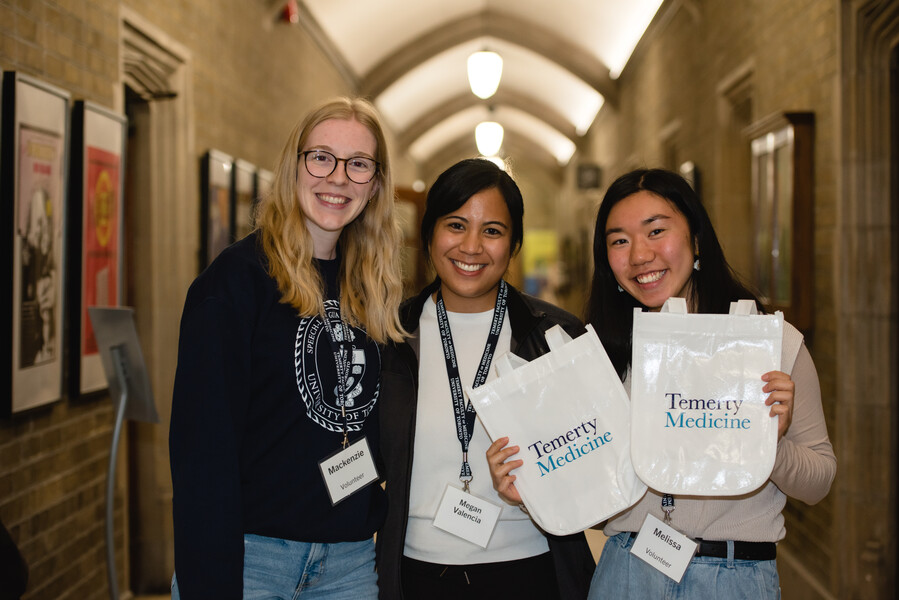 Two volunteers stand with Megan Valencia holding Temerty Medicine tote bags