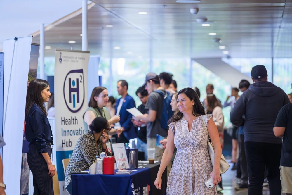 People networking at AcceleratorFest 2024, with the H2i banner in the background